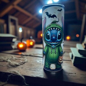 May include: A Halloween-themed tumbler featuring a cartoon character in a green hoodie and holding a jack-o'-lantern. The tumbler has a white background with bats and a moon. The design is printed on a tall, cylindrical cup.