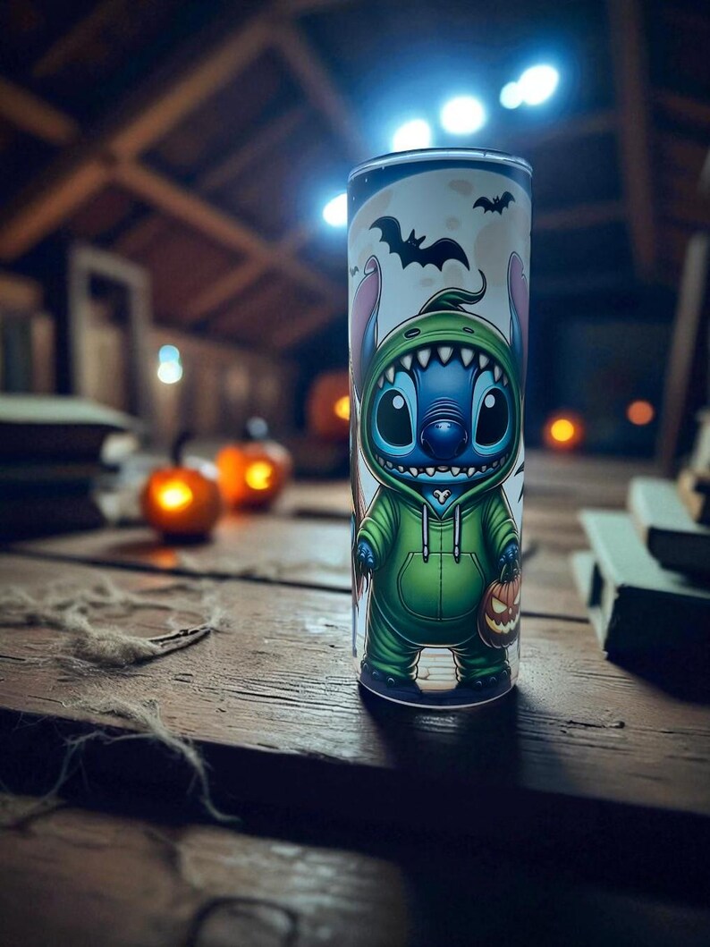 May include: A Halloween-themed tumbler featuring a cartoon character in a green hoodie and holding a jack-o'-lantern. The tumbler has a white background with bats and a moon. The design is printed on a tall, cylindrical cup.
