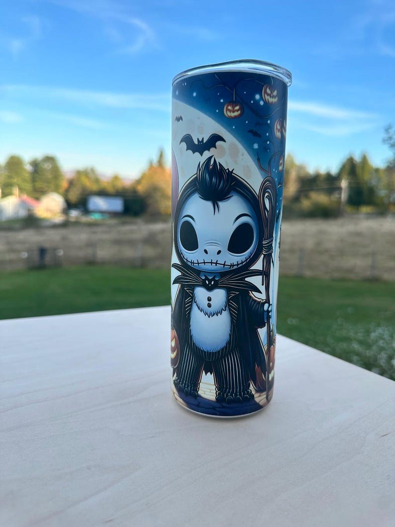 May include: A tall, cylindrical tumbler featuring a cartoon character in a black suit with a white shirt and a bat. The tumbler has a blue background with pumpkins and a full moon. The tumbler is made of stainless steel.