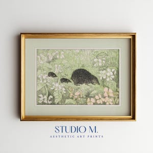 Puede incluir: Impresión artística enmarcada que presenta una ilustración detallada de erizos en un jardín. La obra de arte está en un marco dorado y presenta una paleta de colores verde y blanco. El texto "STUDIO M. AESTHETIC ART PRINTS" está en la parte inferior.