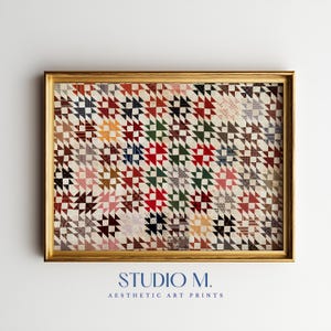Può includere: Una stampa artistica incorniciata con un motivo geometrico a trapunta ripetuto, composto da piccoli triangoli in vari colori tra cui rosso, verde, blu, giallo e marrone su sfondo crema. La cornice è color oro. Il testo riporta STUDIO M.