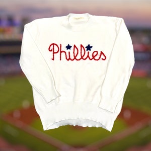 Könnte beinhalten: Weißer Strickpullover mit einem roten gestickten "Phillies"-Logo und zwei blauen Sternen.