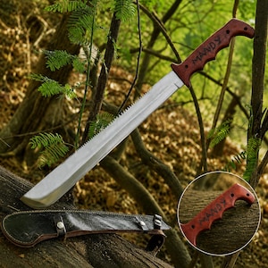Puede incluir: Un machete con una hoja plateada larga y recta con un borde superior dentado y un mango de madera de color marrón rojizo oscuro grabado con el nombre MANDY. La herramienta viene acompañada de una funda de cuero negro con broches de metal plateado.