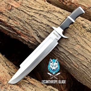 May include: A large, silver, fixed blade knife with a black handle. The blade has a "PREDATOR" inscription and the handle has a silver accent. The knife is resting on a piece of wood.