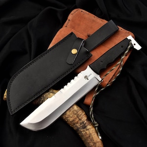 May include: A black leather sheath with a gold button and a large, silver, serrated blade with a black handle. The blade has a skull logo with the text "MAX" on it.