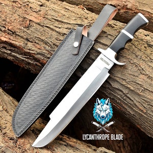 May include: A large, silver, fixed blade knife with a black handle and a leather sheath. The knife has the word "Predator" engraved on the blade. The knife is resting on a piece of wood.