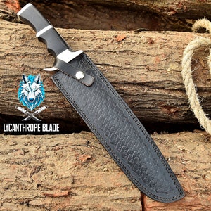 May include: A black leather sheath with a decorative embossed pattern. The sheath has a silver metal buckle and a black handle. The sheath is lying on a wooden surface.  Lycanthrope Blade.
