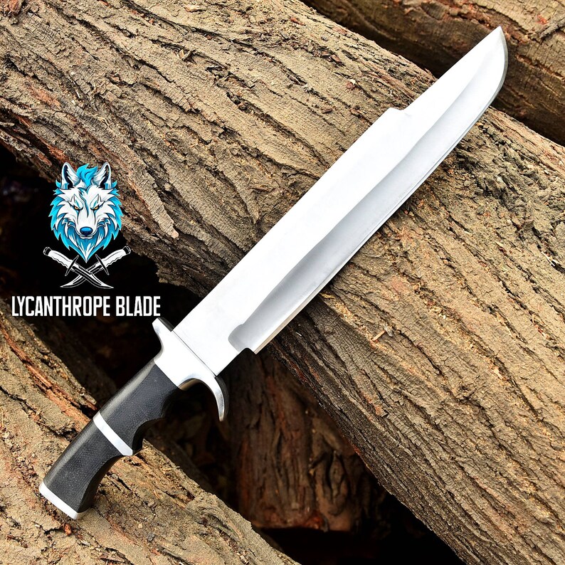 May include: A large, silver, fixed blade knife with a black handle. The knife is resting on a piece of wood. The text "LYCANTHROPE BLADE" is visible in the lower left corner of the image.