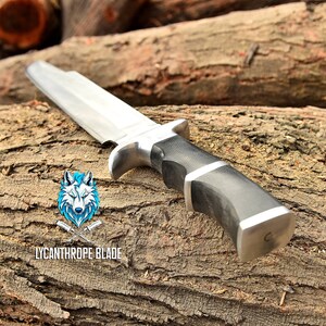 May include: A silver and black hunting knife with a wooden handle. The knife is resting on a piece of wood. The text "LYCANTHROPE BLADE" is visible on the wood.