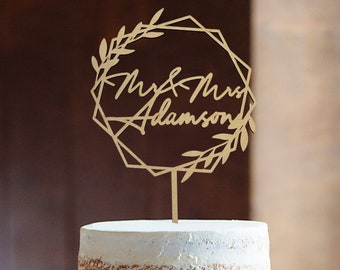 May include: A three-tiered wedding cake with a rustic, naked cake design. The cake is decorated with a simple floral arrangement and a wooden cake topper that reads "Mr. & Mrs. Adamson".