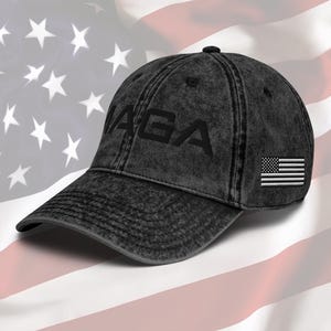 Puede incluir: Una gorra de béisbol negra desgastada con el texto "MAGA" bordado en la parte delantera y un pequeño parche de la bandera estadounidense en el lateral.