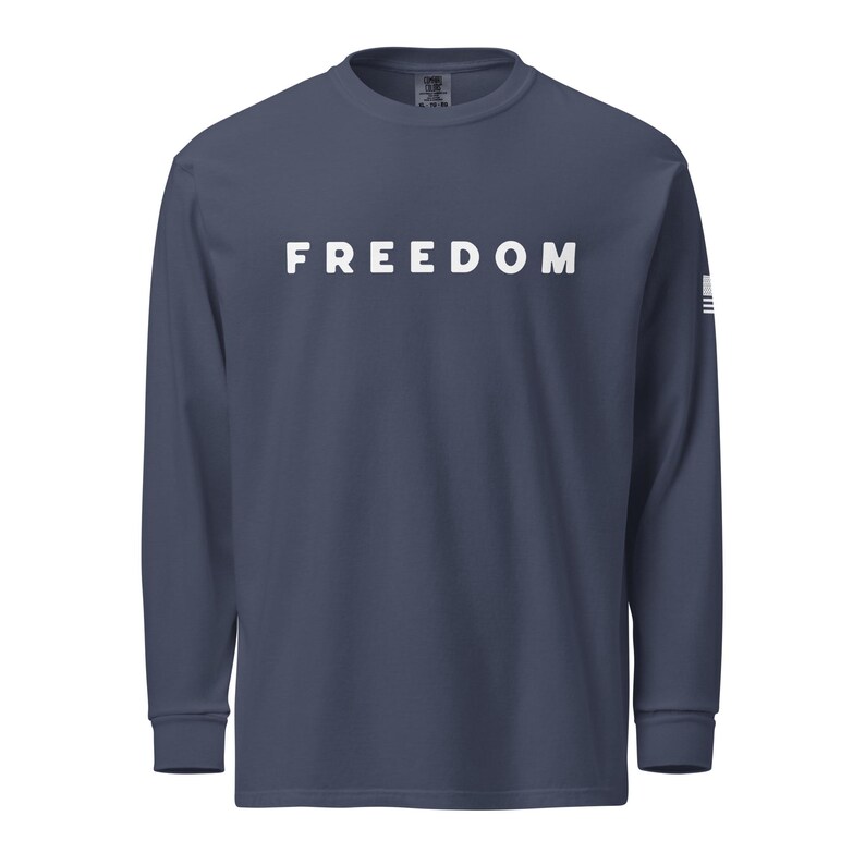 以下が含まれることがあります： 胸に白で「FREEDOM」の文字がプリントされた、ネイビーブルーの長袖シャツ。右袖には小さな白と青のグラフィックがあります。シャツはクルーネックで、ゆったりとしたフィット感です。