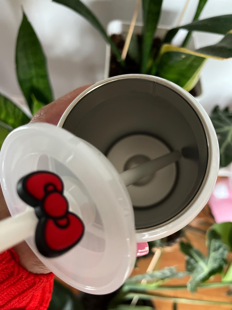 May include: White stainless steel tumbler with a red Hello Kitty bow on the lid. The tumbler has a straw and a clear lid.