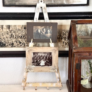 May include: A vintage display featuring framed black and white photographs. Two small easels hold antique photos, with a larger framed photo in the background. A small wooden greenhouse is on the right.