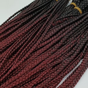 Könnte beinhalten: Ein Bündel ombre-geflechtetes Haar mit einer dunkelburgunder Farbe, die zu Schwarz verblasst. Das Haar ist vorgeflochten und bereit zum Einsetzen.
