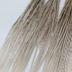 May include: A collection of blonde synthetic dreadlocks in various styles, including straight, braided, and twisted. The dreadlocks are ombre, transitioning from a light blonde to a darker blonde.