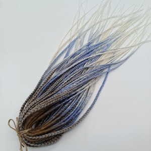 May include: A set of synthetic dreadlocks in brown, blue, and white ombre colors. The dreadlocks are tied together with a brown string.