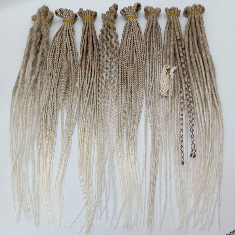 May include: A set of eight ombre synthetic dreadlocks in shades of blonde and white. The dreadlocks are made of kanekalon hair and are approximately 61 cm long.