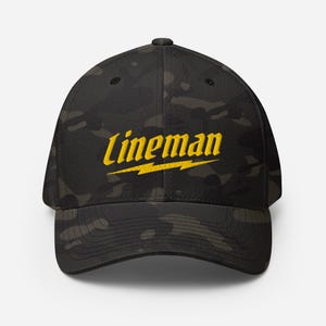 Könnte beinhalten: Eine schwarze Camouflage-Baseballkappe mit dem gelb gestickten Wort "Lineman" und einem gelben Blitz. Die Kappe hat einen gebogenen Schirm und eine strukturierte Passform.
