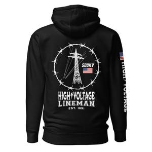 May include: Black hooded sweatshirt featuring a graphic of a high-voltage power tower encircled by barbed wire. The design includes the text "HIGH VOLTAGE LINEMAN EST. 1891" and the American flag. The sleeve displays the words "HIGH VOLTAGE".
