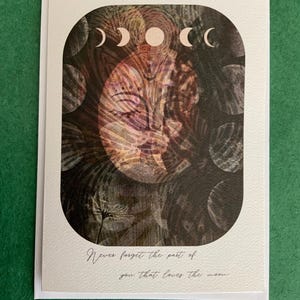 Puede incluir: Una tarjeta de felicitación blanca con una superficie texturizada. La tarjeta presenta una ilustración de las fases lunares y un diseño similar a una cara en tonos marrón, rosa y negro. El texto dice: "Nunca olvides la parte de ti que ama la luna."