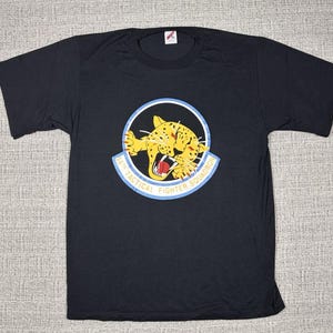 May include: Black t-shirt with a graphic of a yellow and black leopard with the text "52nd Tactical Fighter Squadron".