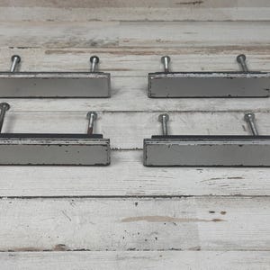May include: Four silver drawer pulls with a rectangular shape and a slightly distressed finish. The pulls have a simple design with a single screw on each side.