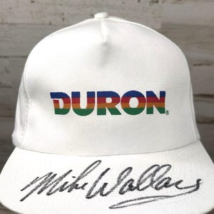 May include: White baseball cap with a rainbow colored "DURON" logo and a black signature that reads "Mike Wallace" on the brim.