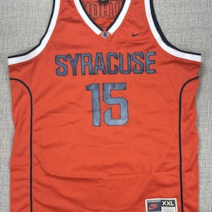 May include: Orange Syracuse basketball jersey with the number 15 in gray. The jersey has a V-neck with white and navy blue trim. The word "SYRACUSE" is across the chest in gray block letters. A Nike logo is visible.