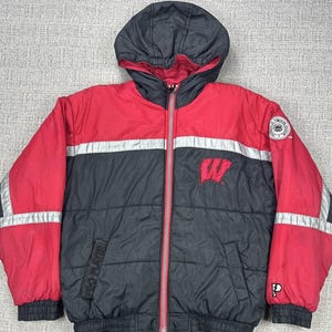 May include: A red, black, and silver hooded puffer jacket with a full-length zipper. The jacket features the letter "W" on the chest and a patch on the upper sleeve. The jacket has a "Pro Player" label.