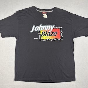 May include: Black t-shirt with the text "Johnny Blaze" in white and yellow, with a red and yellow flame design. The words "New York City" are below the logo. The shirt has a crew neck and short sleeves.