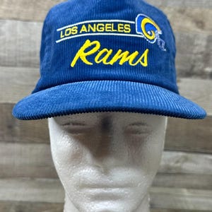May include: A blue corduroy baseball cap with the words "LOS ANGELES Rams" in white and yellow lettering. The cap features a team logo on the right side. The hat is displayed on a white mannequin head.