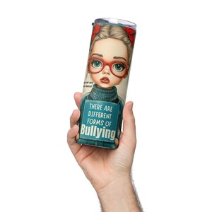 Puede incluir: Un vaso de acero inoxidable con una ilustración de dibujos animados de una niña con gafas rojas y un lazo. El vaso tiene el texto "THERE ARE DIFFERENT FORMS OF BULLYING". El vaso está sostenido por una mano.
