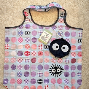 Puede incluir: Una bolsa tote de color azul claro con un estampado de lunares rosas, morados y blancos. La bolsa tiene un ribete gris oscuro y una pequeña bolsa redonda negra con ojos blancos. Una etiqueta dice "My Neighbor Totoro."