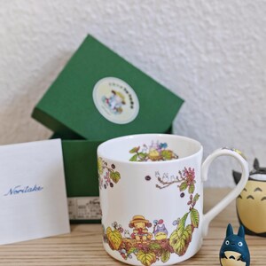 Könnte beinhalten: Eine weiße Keramik-Tasse mit schwarzem Henkel und dem handgeschriebenen Text "But First, Coffee". Die Tasse ist für Heißgetränke gedacht und hat eine glänzende Oberfläche.