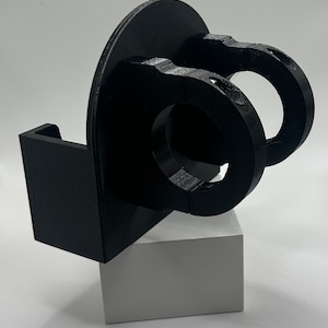 May include: A black 3D printed phone holder with a circular base and a clamp for attaching to a surface. The holder is designed to hold a phone vertically.