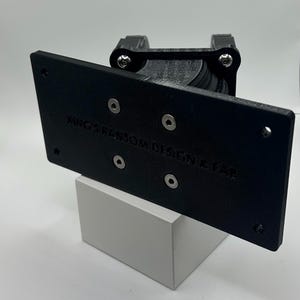 May include: Black 3D printed wall mount with the text "KING'S RANDOM DESIGN & FAB" on the front. The mount is attached to a white block.