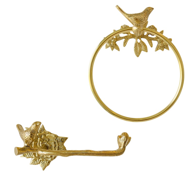 May include: Two brass-colored bathroom accessories: a towel ring and a toilet paper holder. The towel ring is circular with a bird perched on a branch. The toilet paper holder has a branch design with a bird on the left end.
