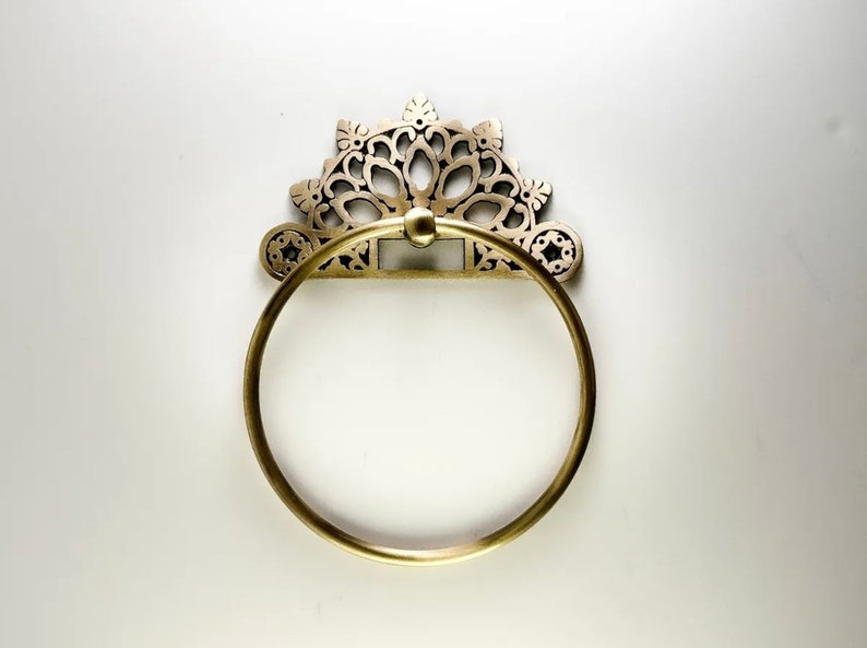 May include: A gold-toned towel ring with a decorative, ornate design. The ring is circular and has a detailed, intricate pattern.
