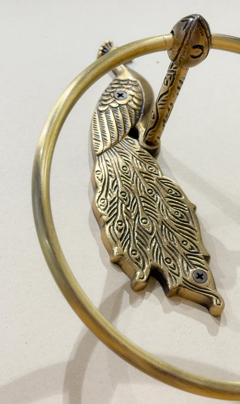 May include: A brass peacock-themed towel ring. The peacock is intricately detailed with etched feathers and a curved tail. The ring is a circular shape, and the fixture is mounted with screws.
