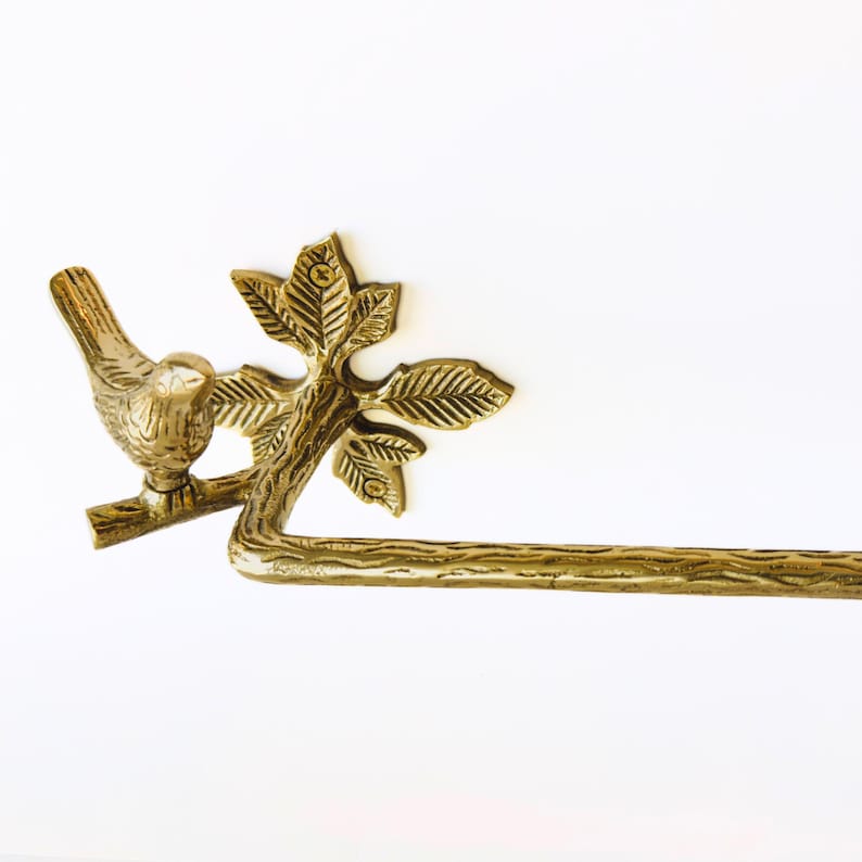 May include: A decorative brass towel bar featuring a bird perched on a branch with leaves. The bar is a horizontal rod, and the design is detailed with a natural, organic aesthetic. The color is a warm, metallic gold.