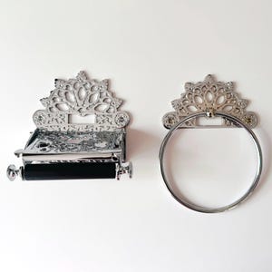 Peut inclure: Un porte-papier toilette chromé avec un rouleau noir et un anneau porte-serviettes circulaire assorti. Les deux accessoires présentent un design métallique ajouré et orné sur le dessus avec des motifs complexes et des trous de fixation.