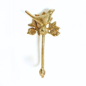 May include: A brass wall hook featuring a detailed bird perched on a floral branch. The hook has a long, slender stem ending in a decorative bud. The bird and floral details are in a gold finish.