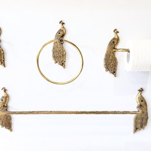 May include: A set of brass bathroom fixtures featuring peacock designs. The set includes a towel bar, a toilet paper holder, a towel ring, and two wall hooks, all with intricate peacock detailing. The fixtures are mounted on a white wall.