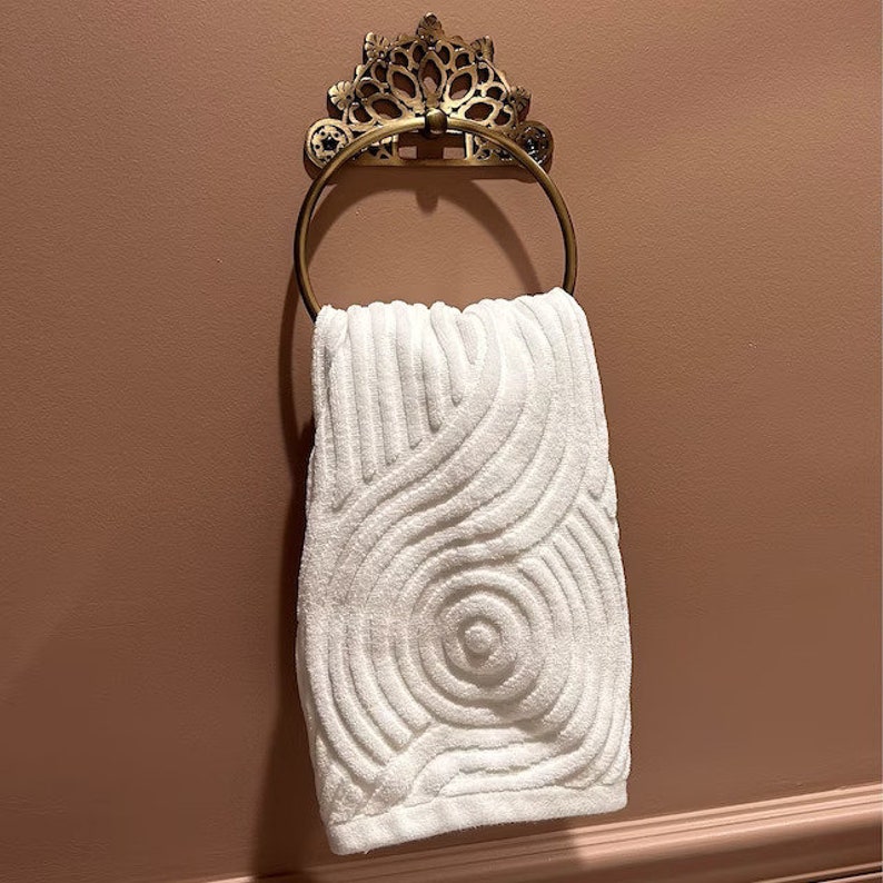 May include: A white towel with a swirling pattern hangs on a gold ornate towel ring.