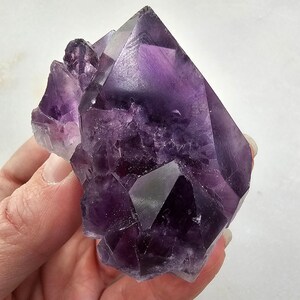 May include: A large, deep purple amethyst crystal cluster with multiple points. The crystal is translucent and has a natural, rough texture.