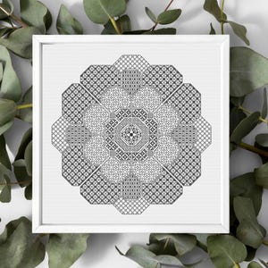 May include: A framed, black and white cross-stitch pattern featuring a complex geometric design. The artwork is composed of various repeating shapes and textures, creating a mandala-like appearance. The piece is set against a white background and framed in a white square frame.