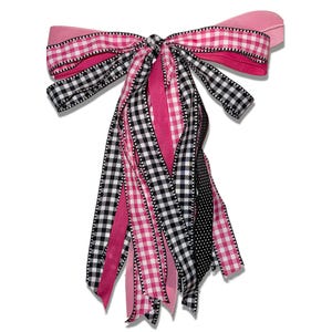 May include: A decorative bow featuring a mix of pink, black, and white ribbons. The bow has a gingham pattern, solid pink, and polka dot ribbons. The bow is tied in the center and has long, flowing tails.