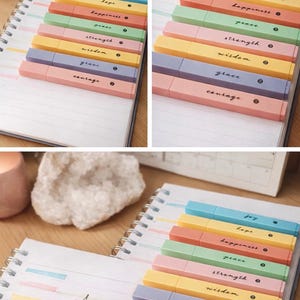 Puede incluir: Un conjunto de resaltadores de colores pastel con palabras inspiradoras como "alegría" y "esperanza" impresas. Los resaltadores están colocados sobre un cuaderno de espiral. También aparece el texto "Jana Rose Finds".