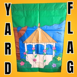 May include: A green and blue garden flag featuring a gazebo design with pink roses and a blue sky background. The flag has the word "YARD FLAG" in large black letters on the sides.